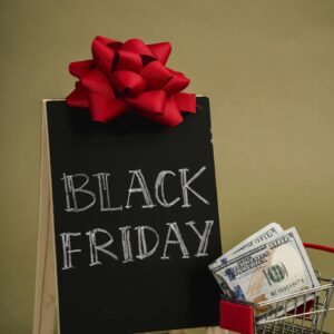 A chalkboard sign with Black Friday written on it and a small shopping cart with dollar bills, ideal for sales promotions.