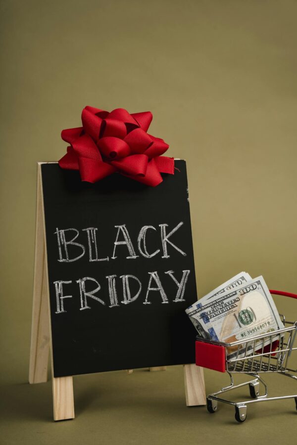 A chalkboard sign with Black Friday written on it and a small shopping cart with dollar bills, ideal for sales promotions.