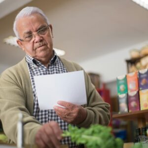 Elderly man shopping in a Portuguese grocery store, holding a paper list.