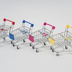 Four miniature shopping carts with colorful handles aligned on a white background for conceptual business imagery.