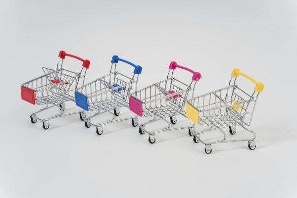 Four miniature shopping carts with colorful handles aligned on a white background for conceptual business imagery.