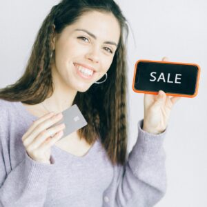 Happy woman promoting online shopping with credit card and sale sign.